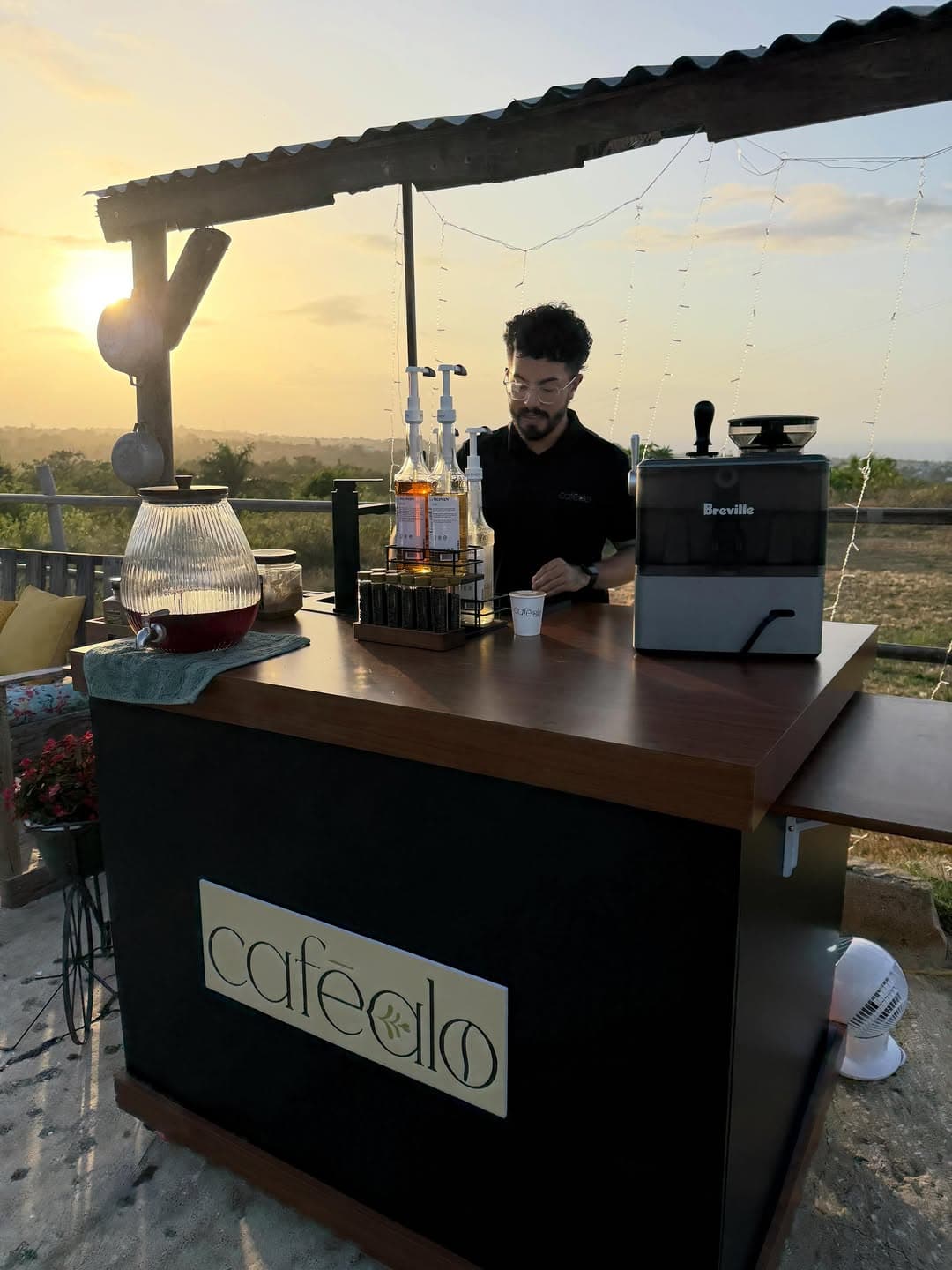 Barista de Caféalo preparando café en la barra móvil durante un atardecer